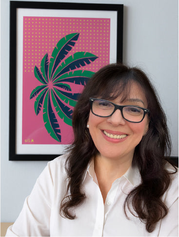Ana smiling in front of her framed artwork with a pink and green design.