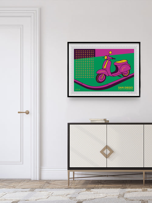 Framed artwork of a purple scooter stamp on a green background above a white cabinet.