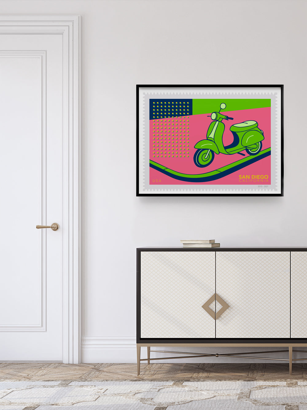 Framed artwork of a green scooter stamp on a pink background above a white cabinet.