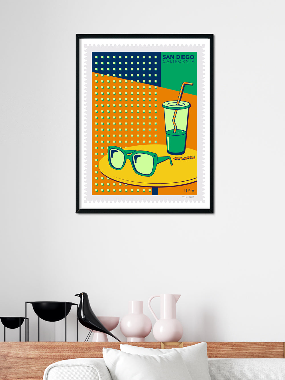 Framed artwork with a colorful design of a glass, sunglasses, and straw on an orange background.