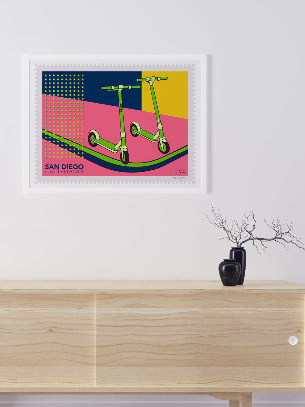 Framed artwork of two scooters on a colorful background above a wooden cabinet.