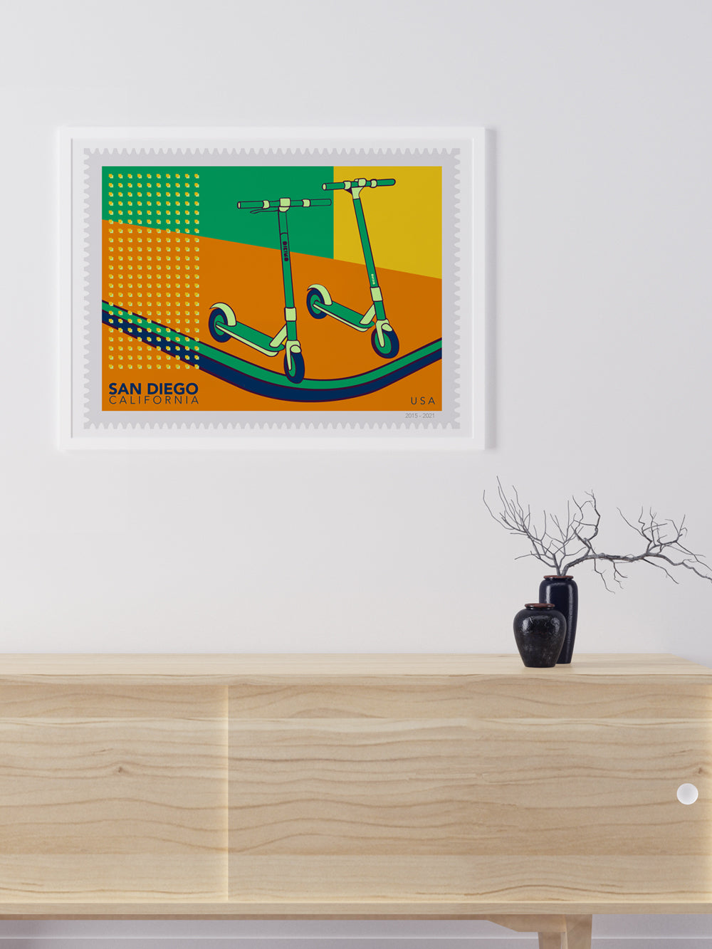 Framed artwork of scooters on an orange background with 'San Diego, California' text, displayed above a wooden cabinet.