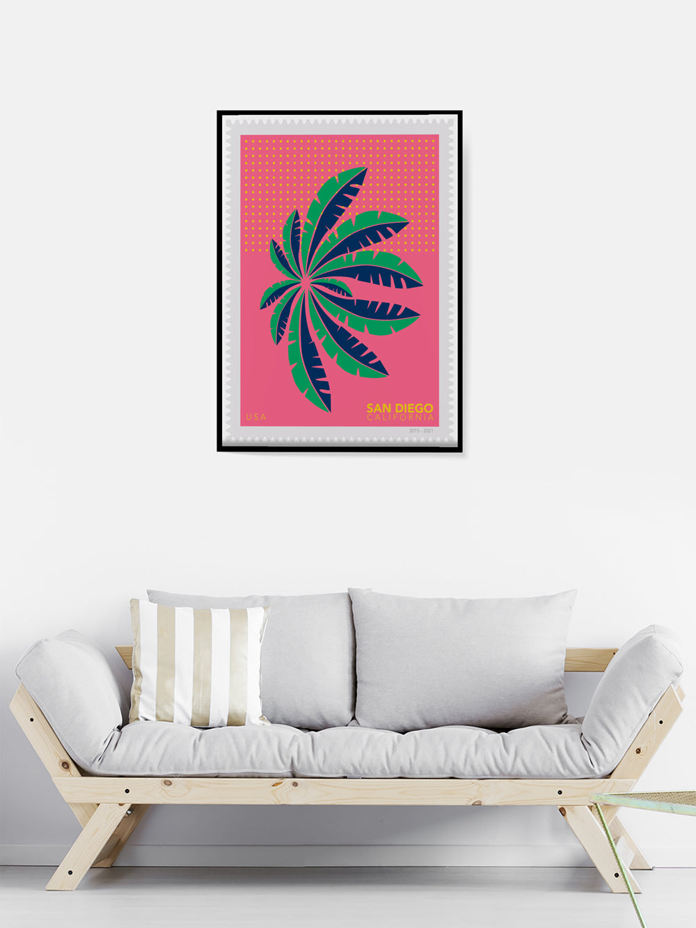 Framed artwork with a palm leaf design on a pink background above a sofa.