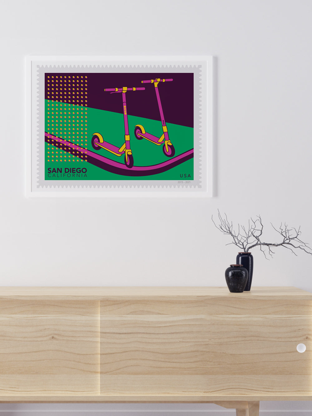 Framed artwork of two pink scooters on a green and purple background, displayed above a wooden cabinet.