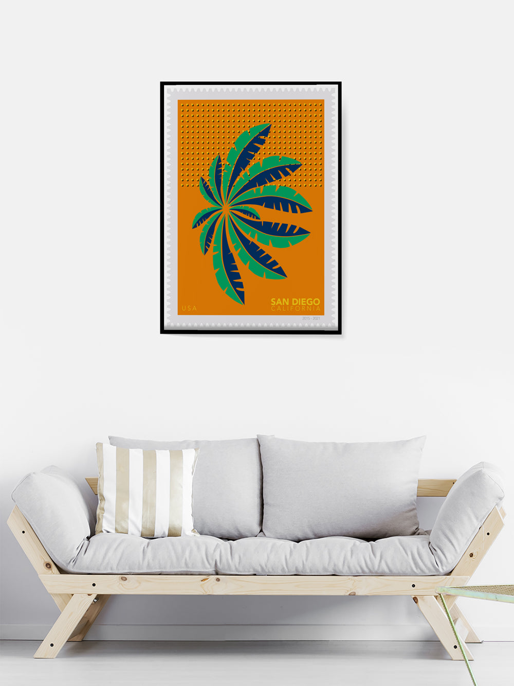Framed artwork of a green leaf design on an orange background above a white sofa.