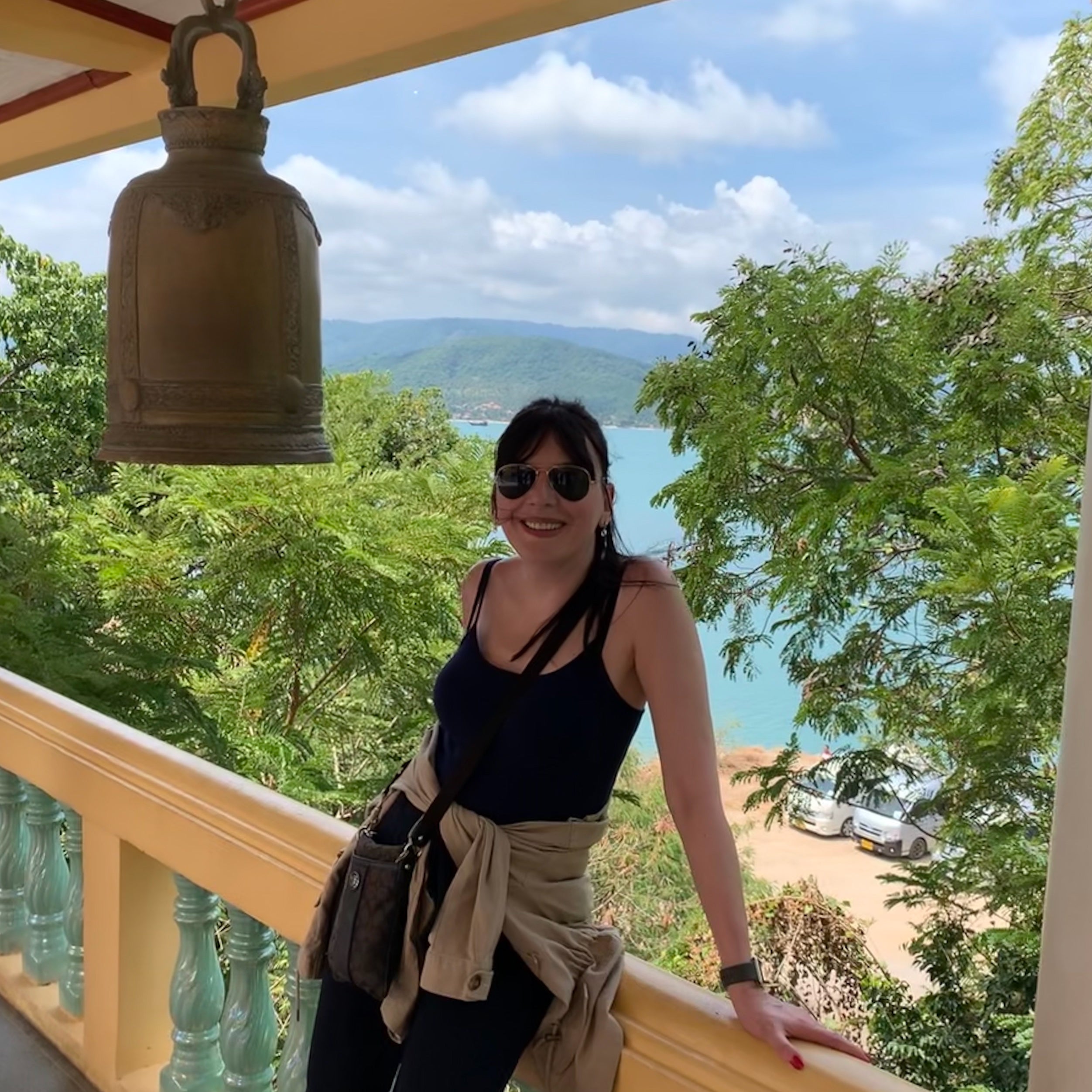 Dragana, the owner of D ART Studio standing on a balcony with a scenic view of trees and water in Koh Samui, Thailand.