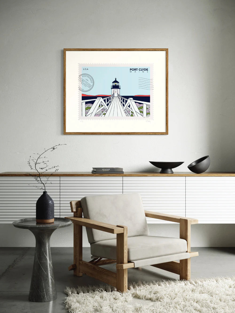 Drawing of Marshall Point Lighthouse in Port Clyde, Maine, in the winter. The drawing looks like a postage stamp with a postmark and words Port Clyde, Maine. Framed on a wall. Ana Hussey art.