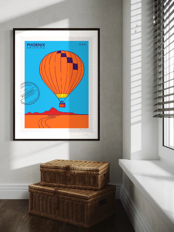 Bright colors drawing of a Phoenix hot-air-balloon ride, floating above the Phoenix desert in this large postage-stamp drawing. Drawing includes words Phoenix Arizona and postmark. Framed on a wall. Ana Hussey art.