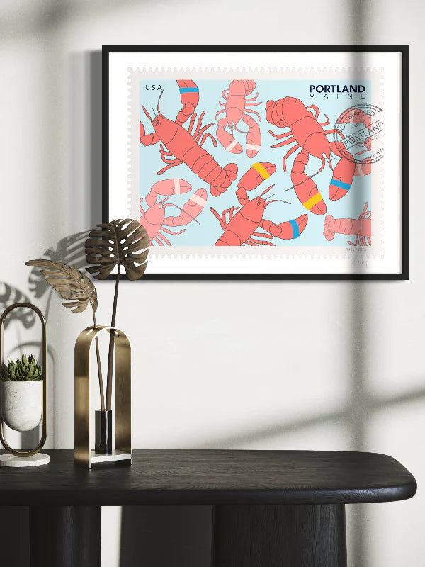 Drawing of lobsters on a blue background. The drawing looks like a postage stamp with a postmark and words Portland, Maine. Framed on a wall. Ana Hussey art.
