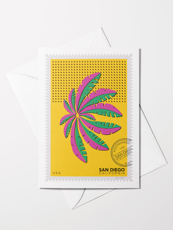 Greeting card with an envelope: a drawing of a green and pink San Diego palm in Mission Bay swaying against a bright yellow sky. The drawing is like a large postage stamp with a postmark and includes words San Diego, California. Ana Hussey art. 