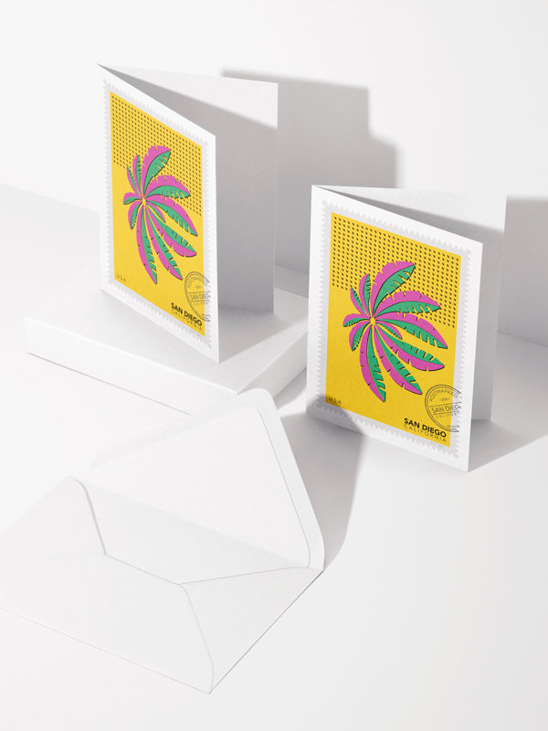 Greeting card with an envelope: a drawing of a green and pink San Diego palm in Mission Bay swaying against a bright yellow sky. The drawing is like a large postage stamp with a postmark and includes words San Diego, California. Two cards and an envelope. Ana Hussey art. 