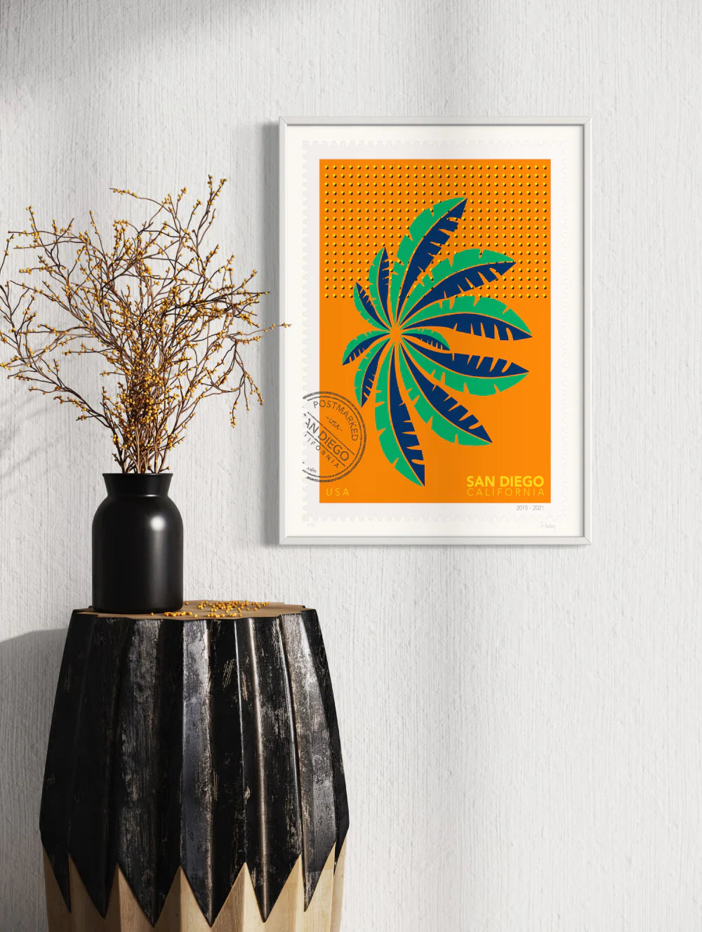 A drawing of a green and blue San Diego palm in Mission Bay swaying against a bright orange sky. The drawing is like a large postage stamp with a postmark and includes words San Diego, California. Framed on a wall. Ana Hussey art.