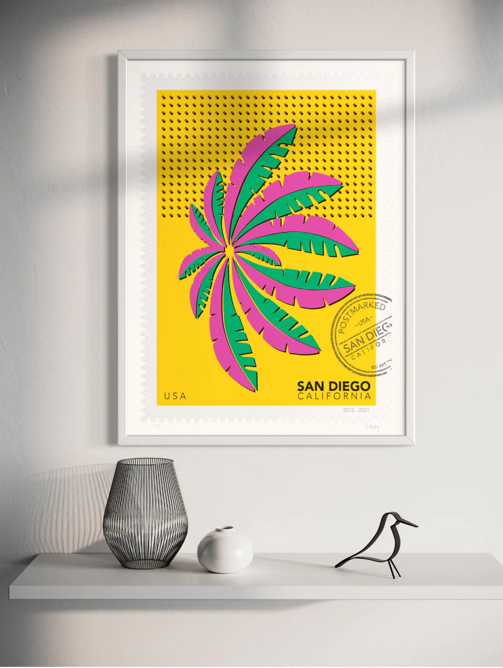 A drawing of a green and blue San Diego palm in Mission Bay swaying against a bright yellow sky. The drawing is like a large postage stamp with a postmark and includes words San Diego, California. Framed on a wall. Ana Hussey art.