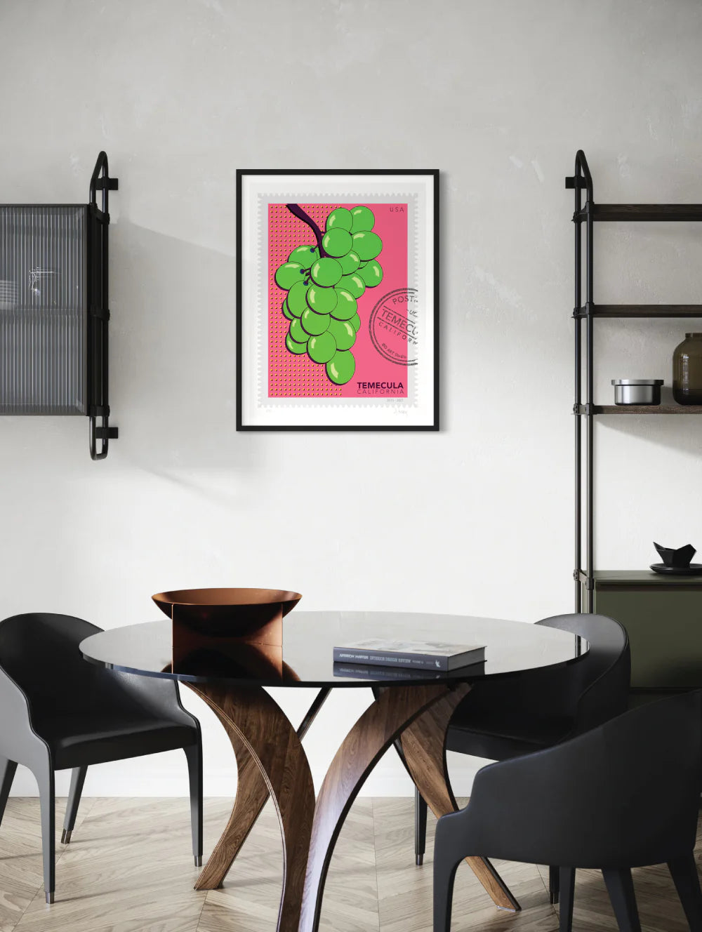 A drawing of green Temecula grapes against a bright pink background. The drawing is like a large postage stamp with a postmark and includes words Temecula, California. Framed on a wall. Ana Hussey art.
