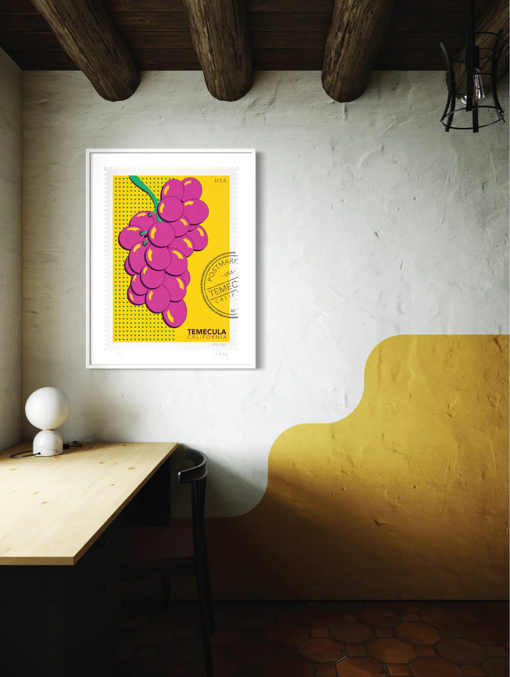 A drawing of pink Temecula grapes against a bright yellow background. The drawing is like a large postage stamp with a postmark that includes the words Temecula, California. Framed on a wall. Ana Hussey art.